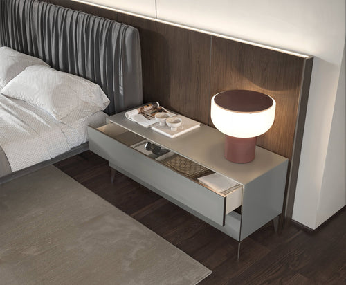 Modern bedroom with a minimalist nightstand featuring a round white lamp, open storage with books and decor, and a striped upholstered headboard.